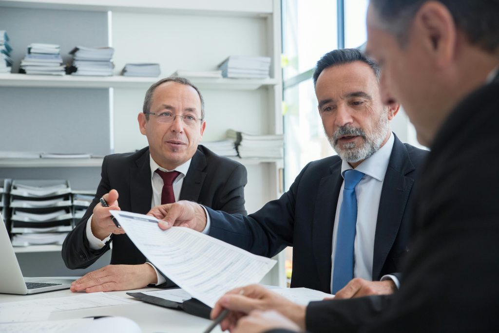 pexels-photo-8428051-8428051 Three businessmen discussing documents in a modern office setting.