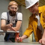 Two individuals collaborating at a table, focused on a project with a tool in use